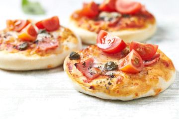 Mini pizzas with ham, cherry tomatoes, mozzarella and capers on bright wooden background. Close up. 