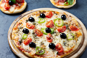 Pizza with mozzarella cheese. cherry tomatoes, jalapeno pepper, capers and black olives on dark stone background.
