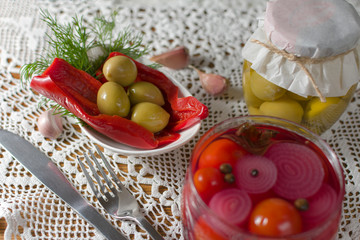 Green pickled olives served on a plate with red pepper and dill. Composition on old style table with handmade tablecloth. Homemade fermented vegetables