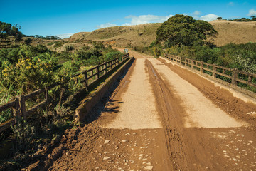 Fototapeta na wymiar Dirt road on rural lowlands with hills and bridge
