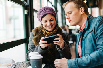 Caucasian couple sitting in a cafe drinking coffee and using a handheld smartphone device
