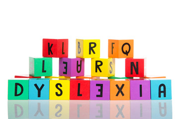 Bright colorful wooden toy blocks stacked on a reflective surface spelling dyslexia. Learning challenges disabilities. E is backwards. Isolated on white background.