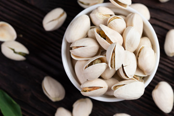  Pistachio in wooden bowl in background with green leaves.