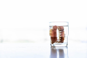 Old dirty denture (fake teethes) steeped in the water in glass close up. Unhealthy oral care.