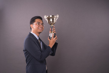 Happy young male intrepreneur or business man holding his gold trophy and celebrating his victory.Studio shot.