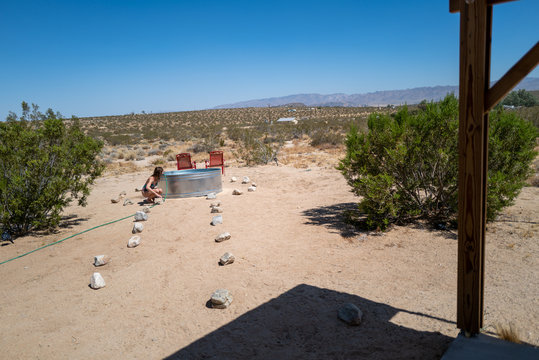 A woman relaxes in a stock tank basin with a hose in an empty desert in Joshua Tree, CA