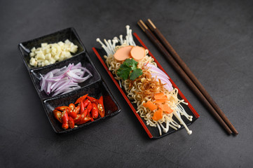 Noodles spicy in Wooden tray with ingredients on black cement background.