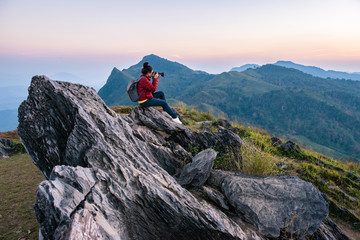 Tourist woman take a photographs of beautiful landscape of Doi Pha Tang in Chiang Rai province of Thailand at sunset. Doi Pha Tang is a mountain cliff over Thai-Laotian border. - obrazy, fototapety, plakaty