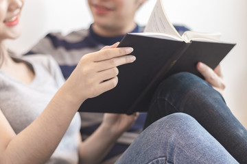 Fototapeta premium Lovely attractive young Asian couple man and woman with happy smile and reading book in romantic moment. Warm heart marriage and lover bonding and relationship. Husband and wife in love photo concept