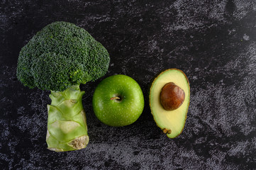broccoli, Apple, and avocado on a black cement floor background.