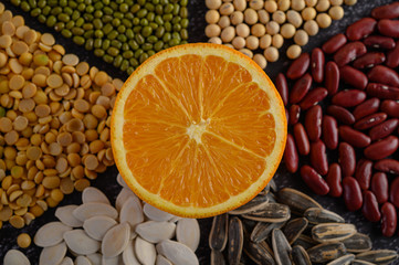 legumes with Orange cut in half on a black cement floor background.