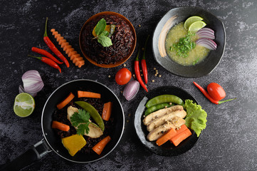 Assorted food and dishes of vegetables, meat and fish on a black stone background. Top view.