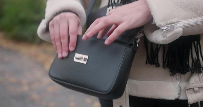 Close up of a black purse around a woman's waist wearing a white warm coat. She opens the handbag and looks for her car or house keys. Professional outdoor steady shot.