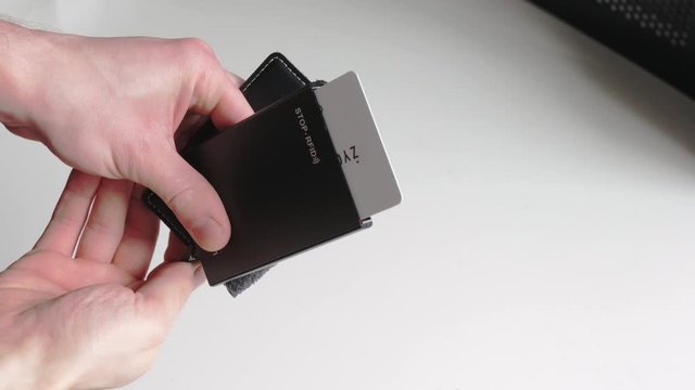 Smart minimalistic wallet, card ejector. Close up man's hand holding black leather and metal wallet ejecting credit cards on isolated white background. Fashionable, slim wallet.