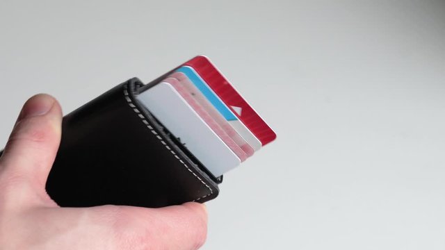 Smart minimalistic wallet, card ejector. Close up man's hand holding black leather wallet ejecting credit cards on isolated white background. Fashionable, slim wallet.