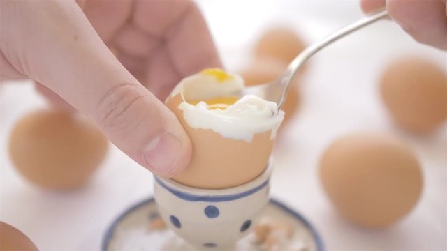 soft boiled egg being eaten on a spoon on white table background with blurred eggs front view
