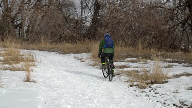 Male cyclist with a backpack is riding a touring bike on a snowy trail in northern Colorado, recreation or commuting concept.