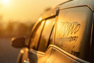 Asian little girl writing or drawing heart symbol on wet mirror of her father SUV car in morning