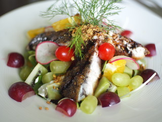 Fried fish with colorful fruit grapes and giwi salad decorated on white plate