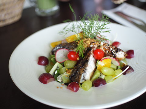 Fried fish with colorful fruit grapes and giwi salad decorated on white plate