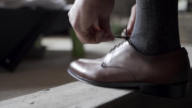 Man tying his brown dress shoe, side shot dramatic lighting