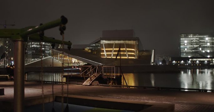 Cinematic gimbal wide angle 4K shot with slow parallax motion of empty playground in front of the illuminated Oslo Opera and Ballet House and Edvard Munch Museum Lambda, at night in Oslo Norway.