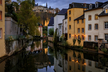 Fototapeta na wymiar Pastel houses reflecting in Alzette river in Luxembourg old town, UNESCO World Heritage Site and the city wall at sunset