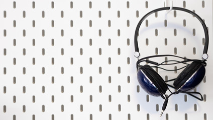 Wallpaper of a black headphone hanging from a  white peg board on the wall 