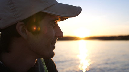 Attractive cheerful Man weaaring cap Relaxing On Sea Boat At beautiful Sunset. Man Sailing On Boat On Vacation Nature Travel Leisure And Summer Concept.