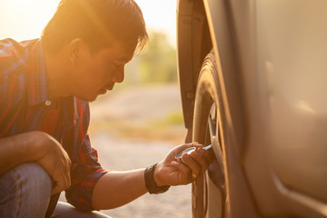 Asian man checking air pressure and filling air in the tires of his car