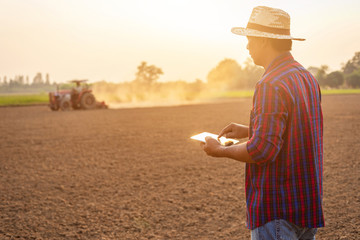 Asian young farmer working and holding tablet in the empty land. Prepare the soil and planning to...