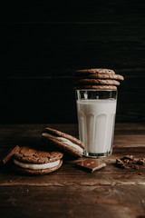 a glass of milk stands on a wooden table near a chocolate chip cookie