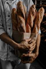 baker's hands are holding a craft baguette with baguettes on a dark background