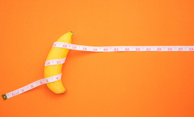 Yellow banana with measurement tape on orange background. Men penis size concept with empty free...