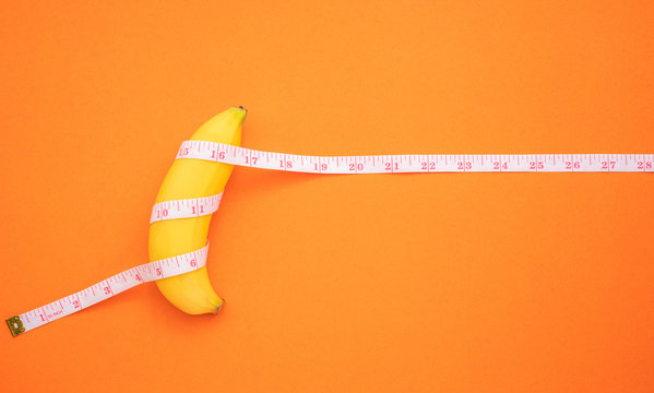 Yellow banana with measurement tape on orange background. Men penis size concept with empty free space for text or design