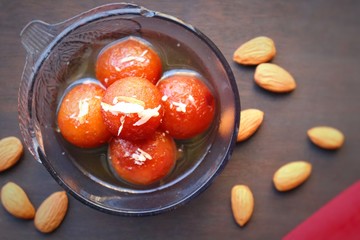 Gulab Jamun in a glass bowl on wood background with Almonds