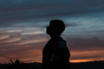 Silhouette of a young Indian boy looking up towards the sky during the sunset at Wankaner, Gujarat, India