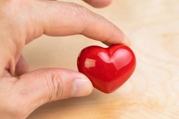 Fototapeta premium Hand holding red heart shape with fingers on wooden background using as love symbol, health care, happy relationship or Valentine day event