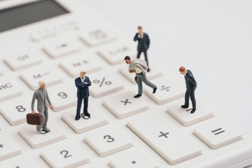 Miniature people businessmen figure standing on white calculator on white background using as teamwork ,business performance success, profit and loss in accounting or company management concept