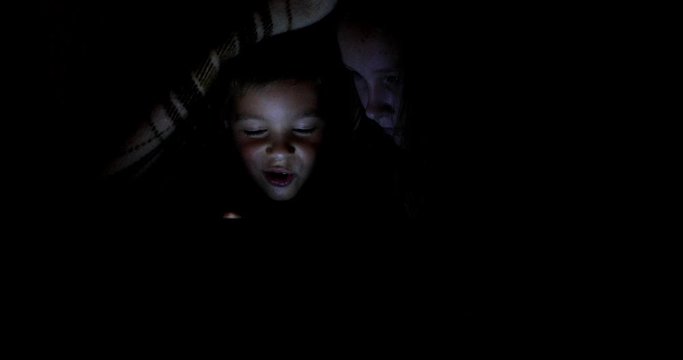Little girl and boy watching content on her smartphone. The pitfalls of social networks. The childern secretly communicates over the Internet at night. Viewing inappropriate content.