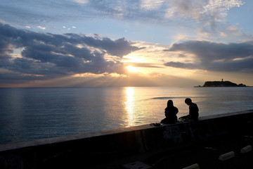 Naklejka na ściany i meble young girl and boy sitting on the coast watching sunset and sea horizon. At Kamakura in Japan