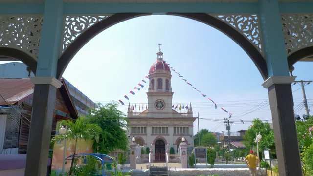 The stunning view of a cathedral coming out of park in Santa Cruz, Thailand with banderitas streamed from the bell tower to the trees - Wide shot