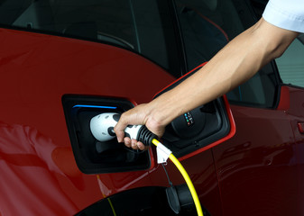 Hand of man holding plug for charge electric power into Battery of Electric car on charge station electric mobility environment friendly with copy space.