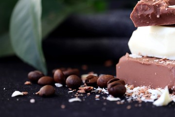 Stacked pieces of milk chocolate and white chocolate bar on black background with coffee beans.