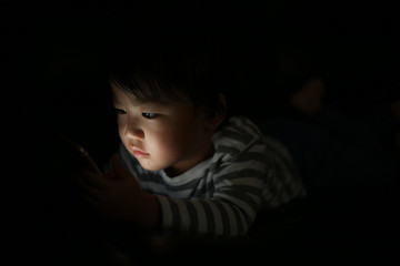 暗い中でスマートフォンを使う男の子