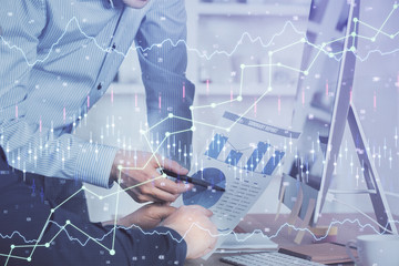 Double exposure of chart with businessman typing on computer in office on background. Concept of hard work.