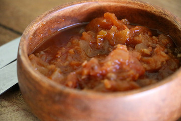 Close-up of a small wooden bowl on a table top containing tomato salsa dip relish