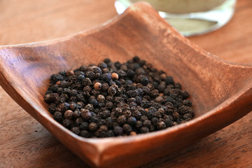 Close-up of small wooden bowl on table containing black peppercorn balls