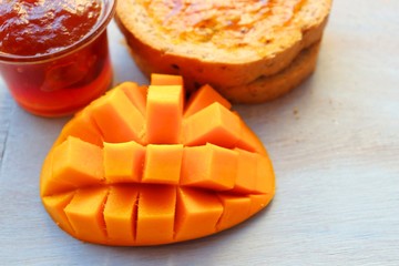Nutritious Breakfast of fresh multigrain bread and mango jam with a slice of fresh mango on a wooden plank