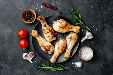 grilled chicken legs with spices on a black plate on a stone background